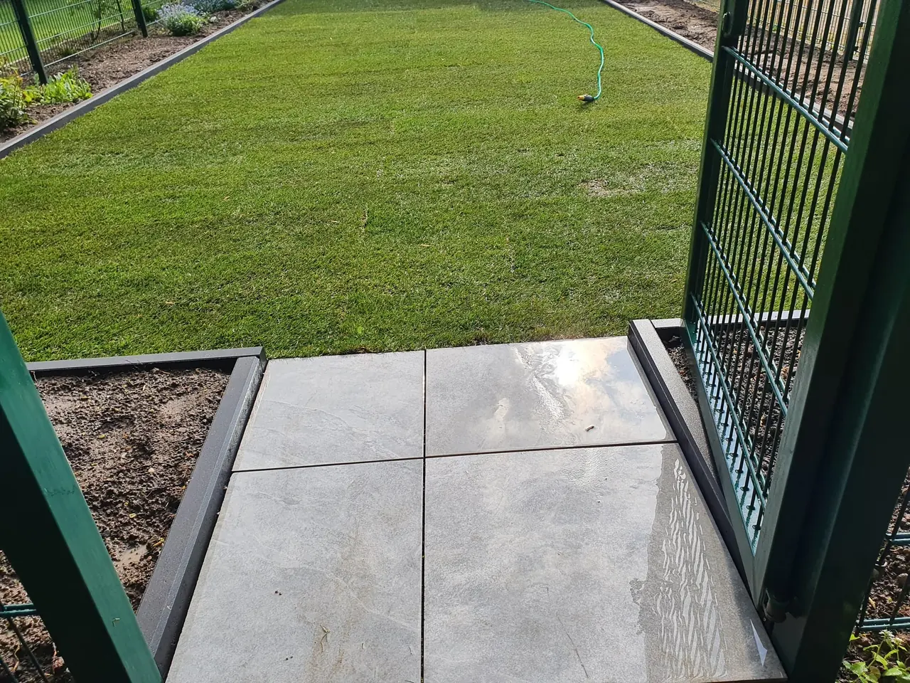 Präzise verlegte Terrassenplatten im Großformat mit stabiler Rasenkanten-Einfassung und modernem Zaunsystem