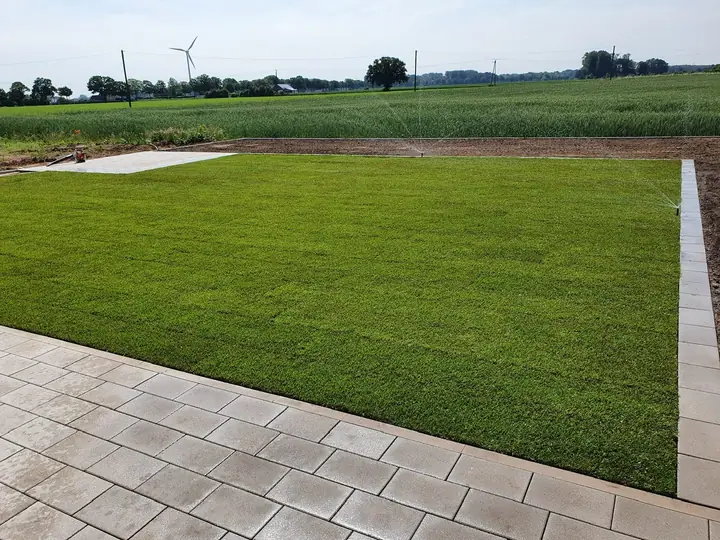 Weite Gartenanlage mit gepflegtem Rasen und hellem Pflasterläufer als Begrenzung