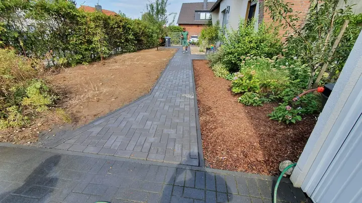 Gepflasterter Gartenweg mit beidseitig angelegten Rindenmulch-Pflanzbeeten
