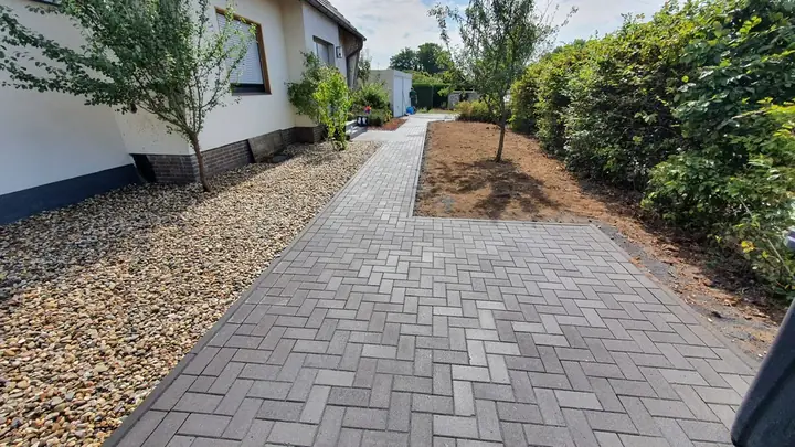 Gartenweg aus hellem Pflasterbelag, gesäumt von Pflanzbeeten und Gehölzen