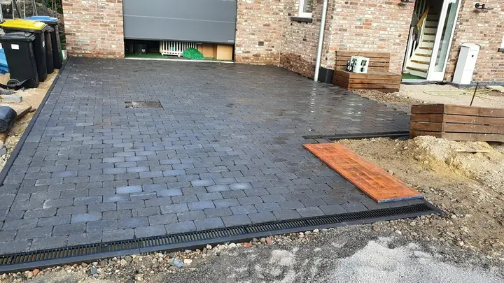 Dunkle Pflasterfläche mit präzisem Fugenbild vor einem Carport